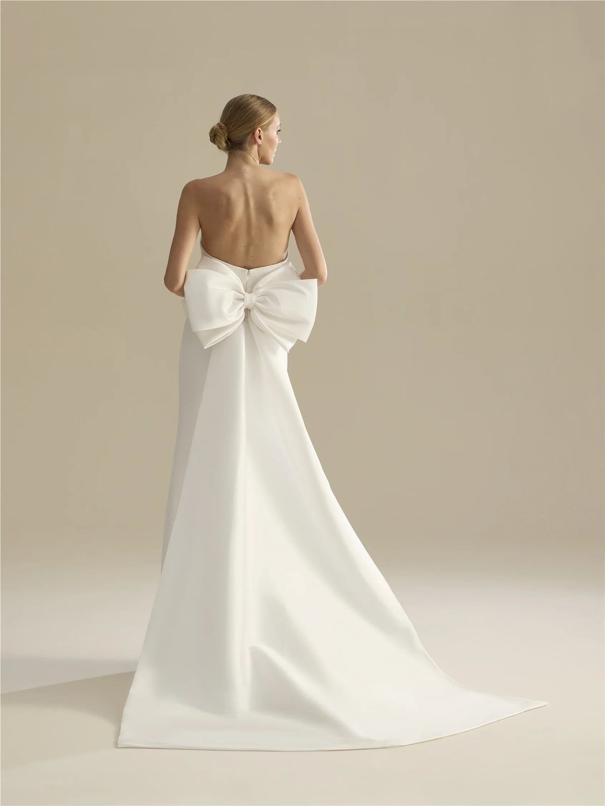 Woman wearing an elegant white backless wedding gown with a large bow detail at the back and trailing train